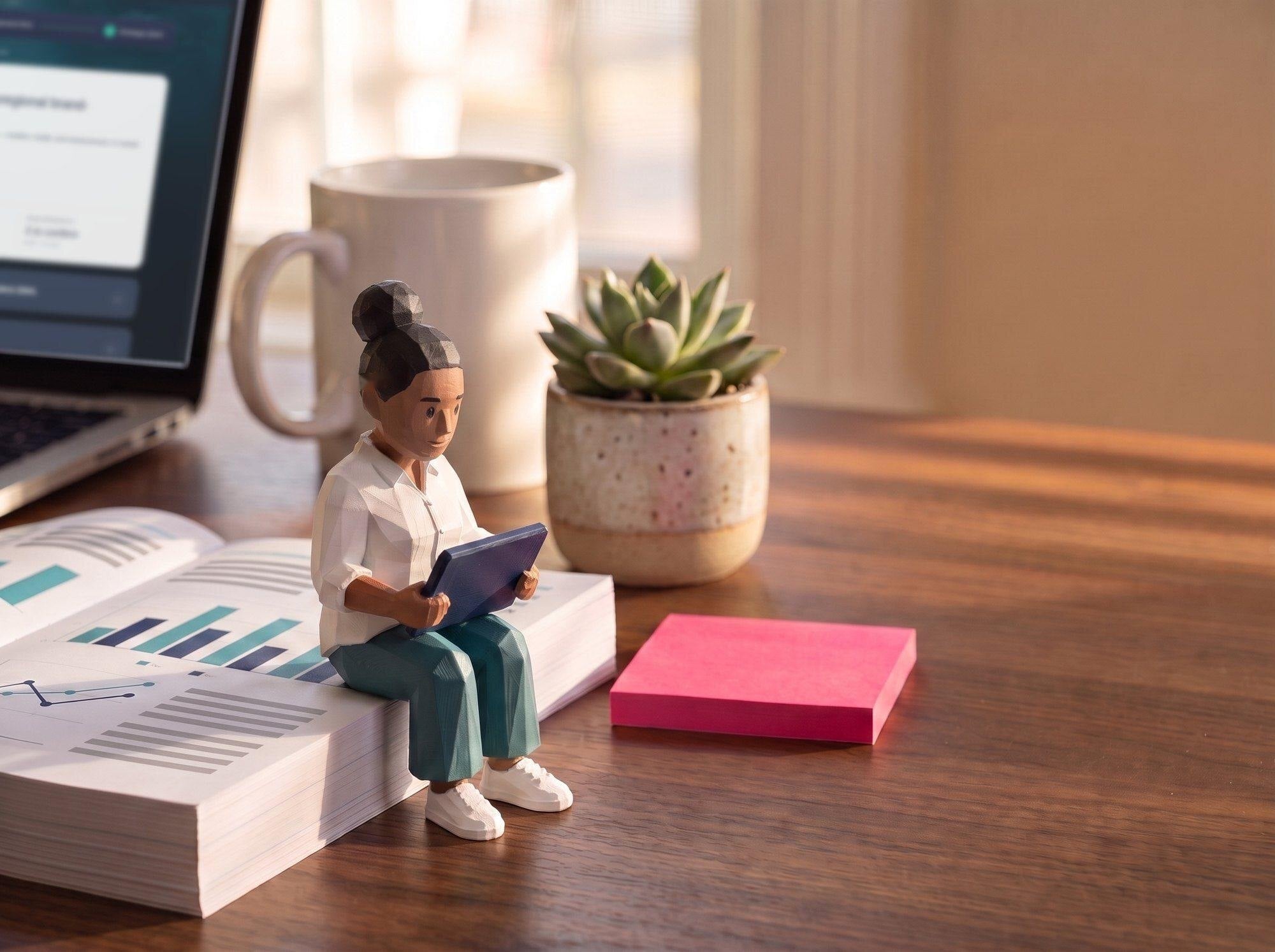A polybit figure of an account manager sitting on a printed media report on a desk, reading a tablet, beside a pink sticky note