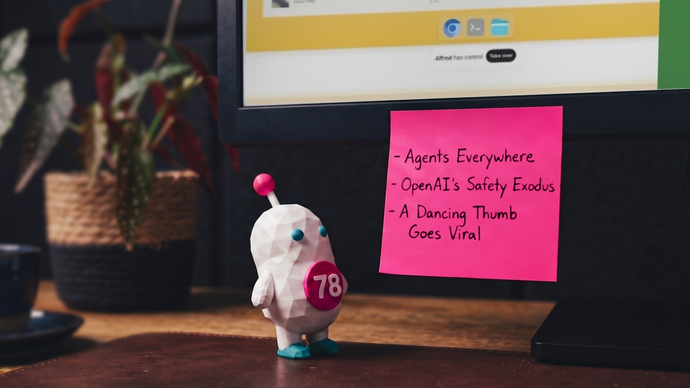 Siggy, the Signal78 figure, beside a pink sticky note on a monitor listing the week’s topics