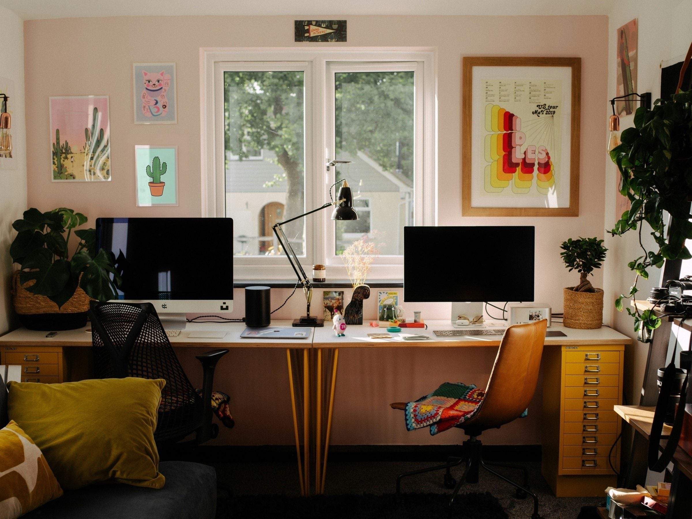 A bright agency studio with two desks, plants and framed prints, and a small Siggy standing by the desk lamp